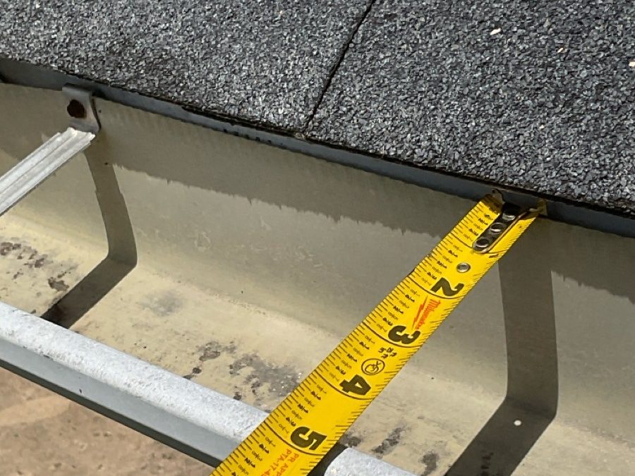 Tape measure held across a gutter and drip edge to record dimensions during an inspection