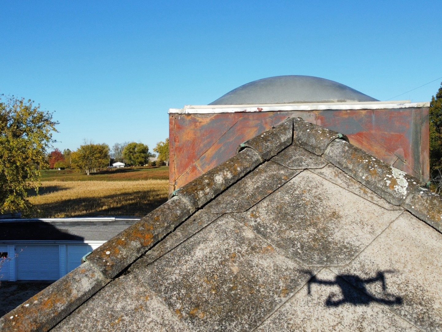 Ridge-level drone view of an aged rural roof showing lichen growth and weathered metal flashing